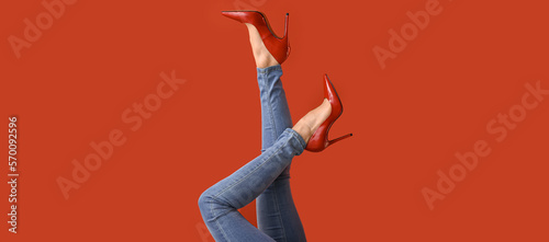 Tableau sur toile Legs of young woman in red high-heeled shoes and jeans pants on color background