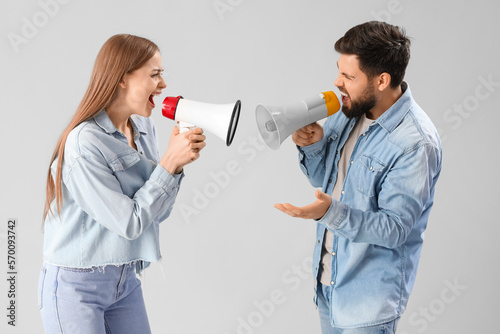 Young couple shouting into megaphones on grey background