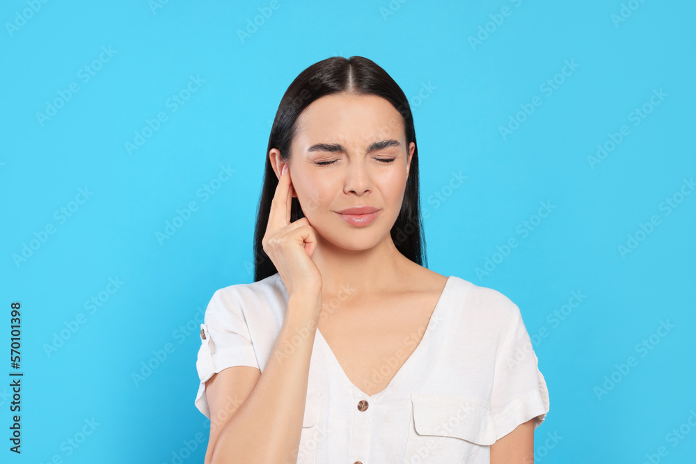 Young woman suffering from ear pain on light blue background Young woman suffering from ear pain on light blue background
