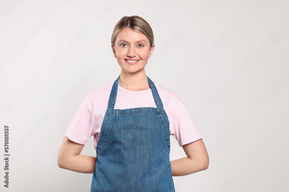 Beautiful young woman in denim apron on light grey background Beautiful young woman in denim apron on light grey background