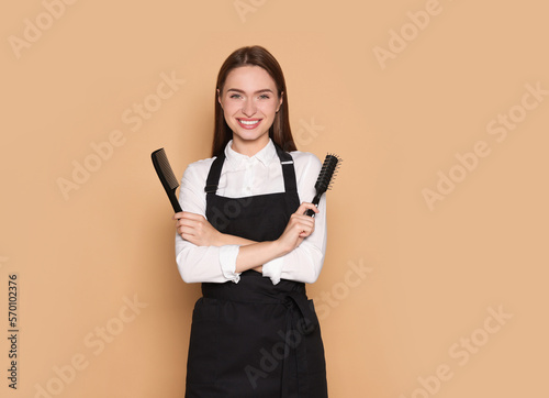 Portrait of happy hairdresser with brush and comb on beige background. Space for text