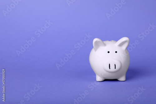 Ceramic piggy bank on purple background, space for text. Financial savings