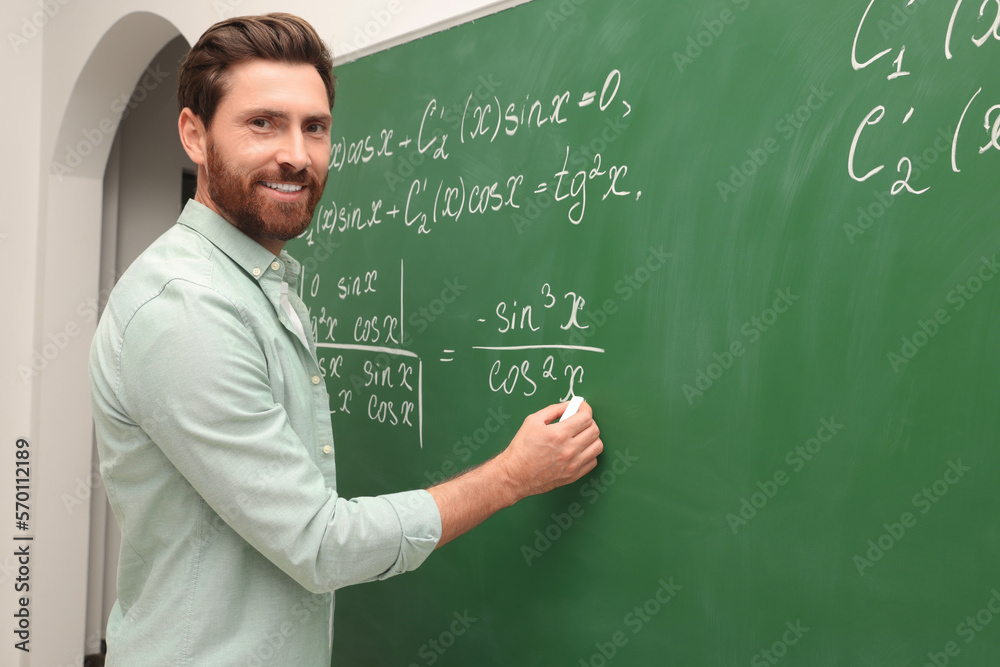Happy teacher explaining mathematics at chalkboard in classroom Happy teacher explaining mathematics at chalkboard in classroom