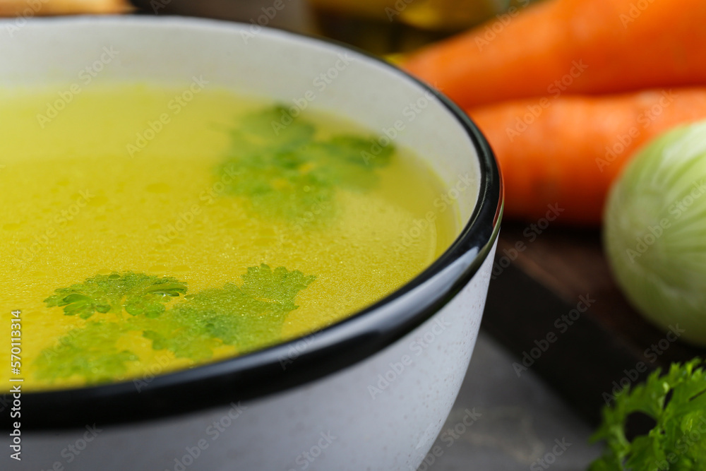 Delicious chicken bouillon with parsley on grey table, closeup Delicious chicken bouillon with parsley on grey table, closeup