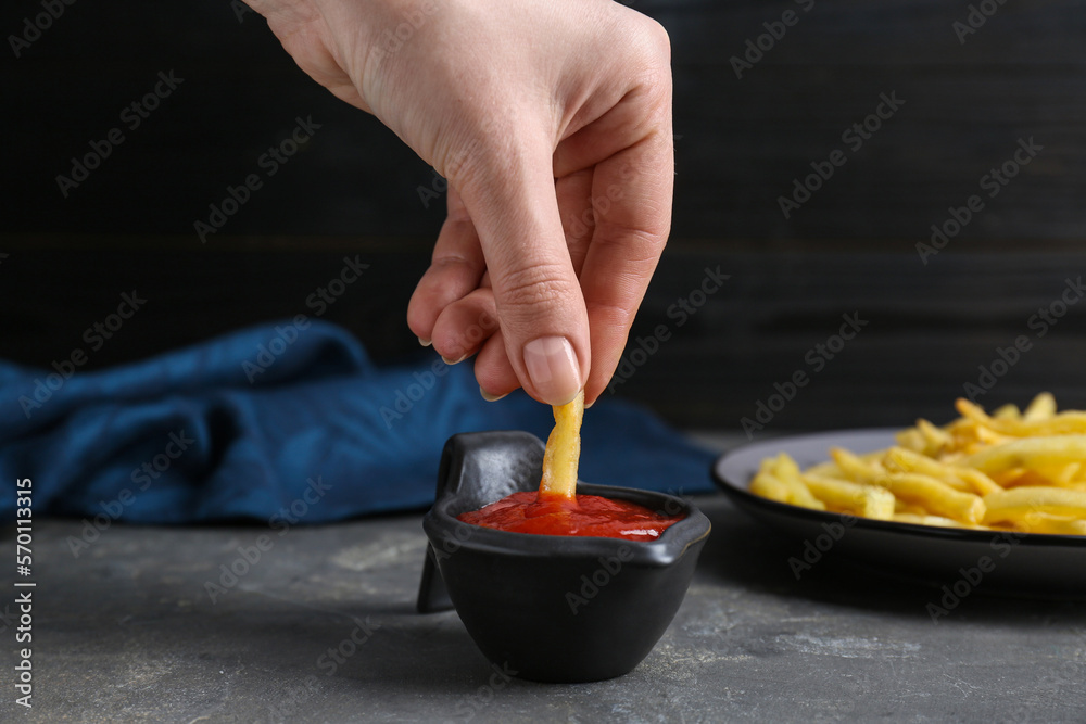 Woman dipping french fry into ketchup at grey table, closeup Woman dipping french fry into ketchup at grey table, closeup
