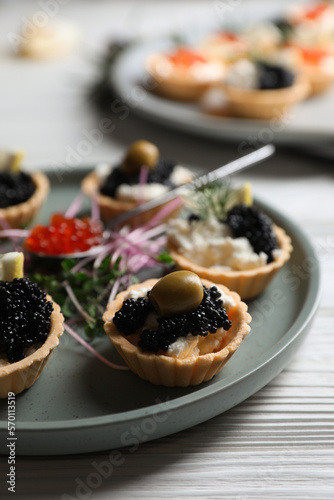 Delicious tartlets with caviar and cream cheese served on white wooden table, closeup