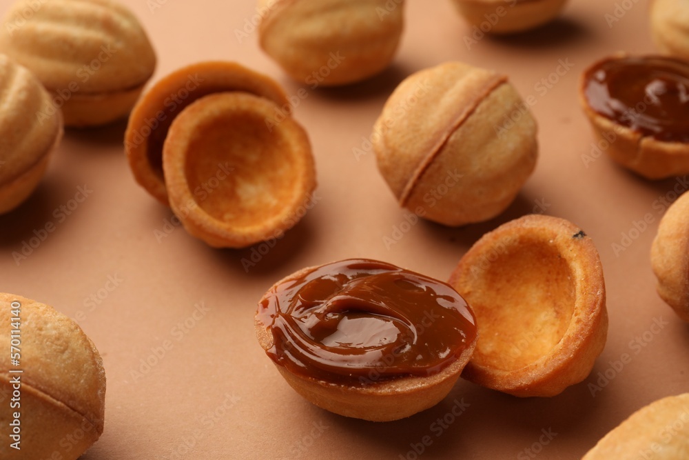 Homemade walnut shaped cookies with boiled condensed milk on pale brown background, closeup