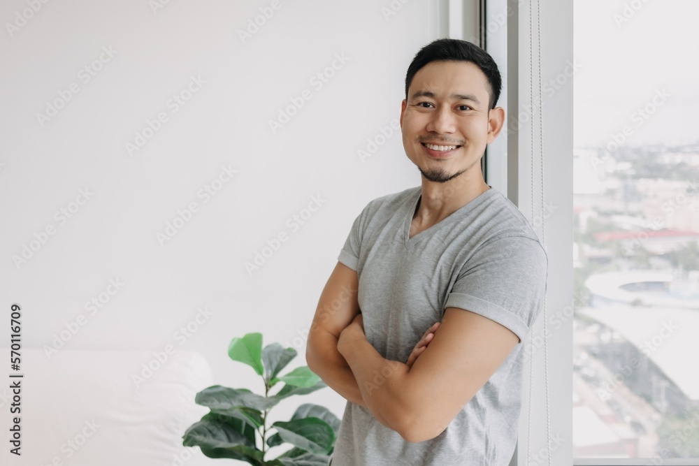 Ordinary happy life smile face asian man stand by the window in his apartment. Ordinary happy life smile face asian man stand by the window in his apartment.