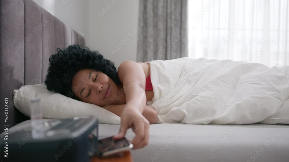 Beautiful African American woman takes smartphone in bed at morning. Smiling girl scrolling social media feed. Slow motion wireless connection and communication shot. Side view bedroom in apartment Beautiful African American woman takes smartphone in bed at morning. Smiling girl scrolling social media feed. Slow motion wireless connection and communication shot. Side view bedroom in apartment