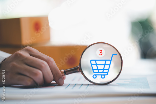 Startup or small business entrepreneur holding a magnifying glass, and the shopping cart icon and ordering order, Internet shopping, online shopping on the Internet, SME, shipping boxes, e-commerce