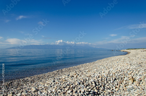 The shore of the lake with pebbles. Calm blue water and clear sky.