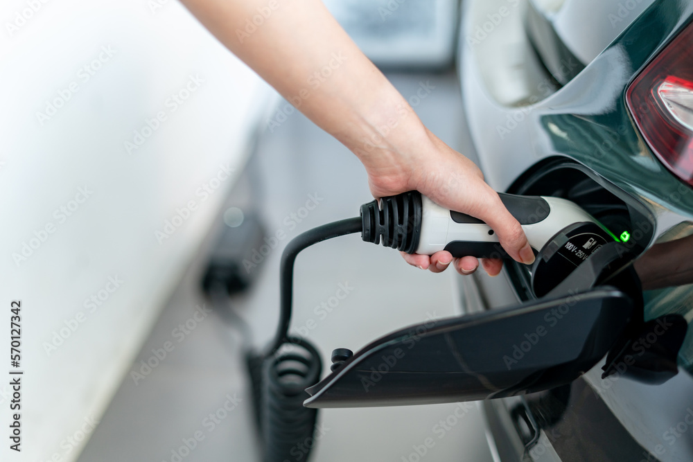 Woman plugged cable charging an electric car at home.