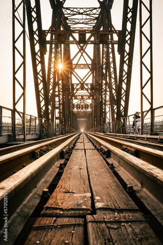 Fototapeta Naklejka Na Ścianę i Meble -  Train tracks lead downwards over a long metal bridge. There is a warm evening atmosphere.