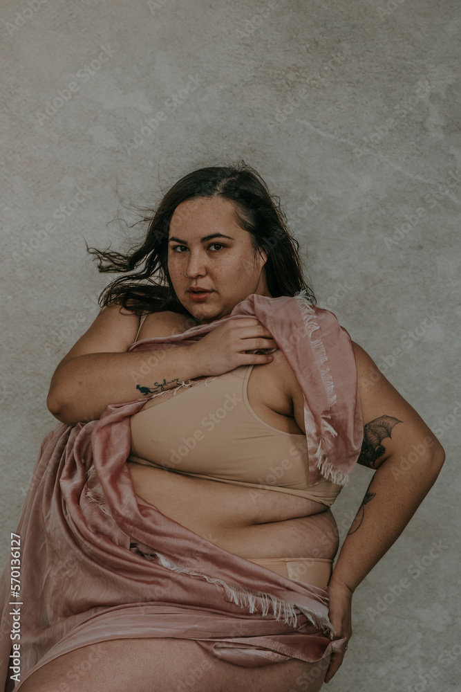 Naklejka premium close-up plus size metis woman looking at camera holding pink fabric wearing nude bra looking at camera
