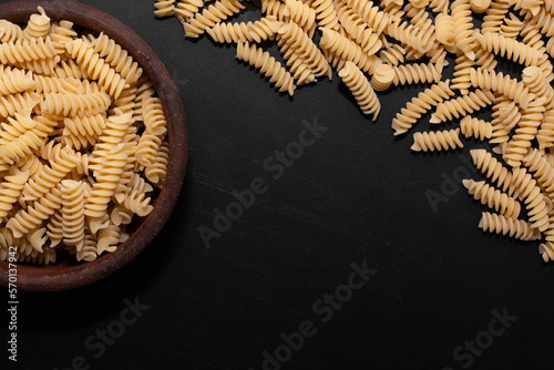  raw pasta shaped inside plate and outside on black table with space for text with white light