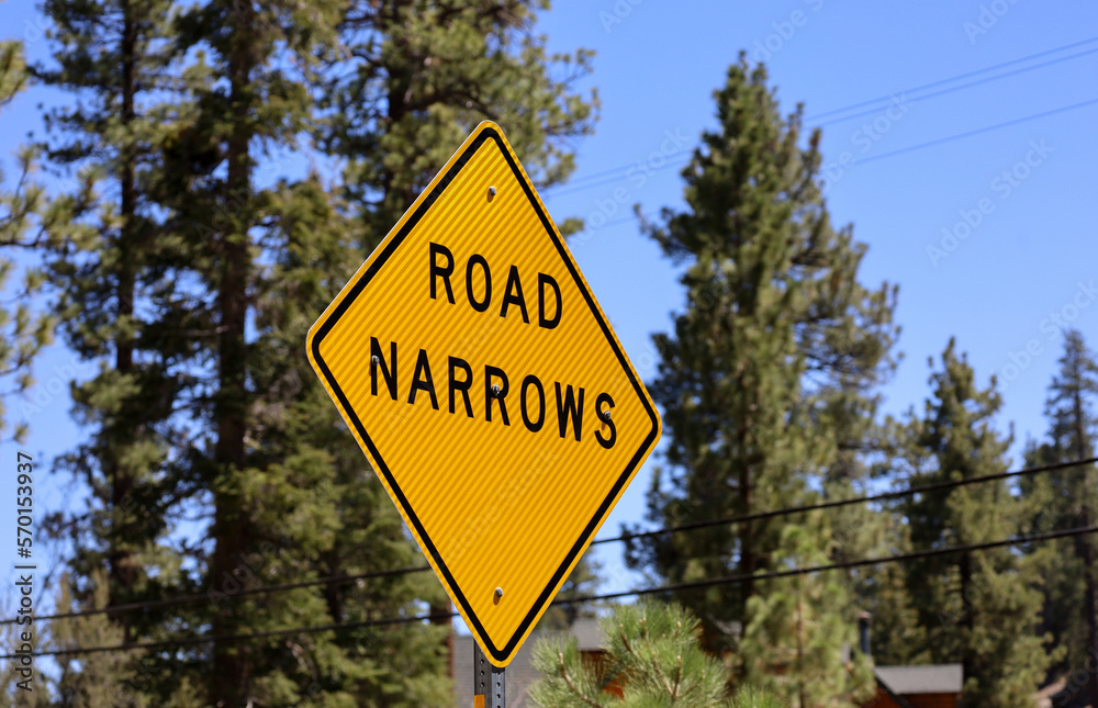 A bright yellow Road Narrows sign.