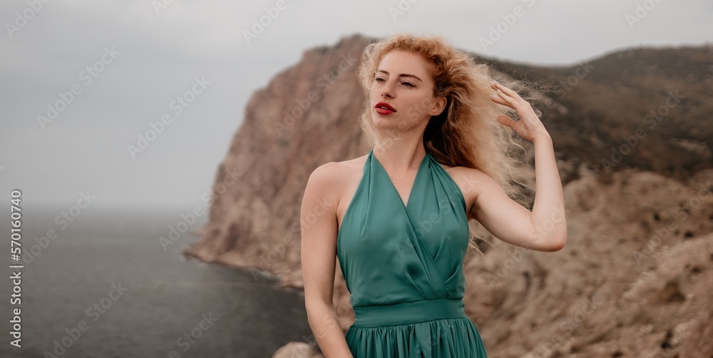 Redhead woman portrait. Curly redhead young caucasian woman with freckles looking at camera and smiling. Close up portrait cute woman in a mint long dress posing on a volcanic rock high above the sea Redhead woman portrait. Curly redhead young caucasian woman with freckles looking at camera and smiling. Close up portrait cute woman in a mint long dress posing on a volcanic rock high above the sea