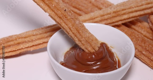 A close up to a caramel plate with somebody dipping a Churro into it while the camera going around.
