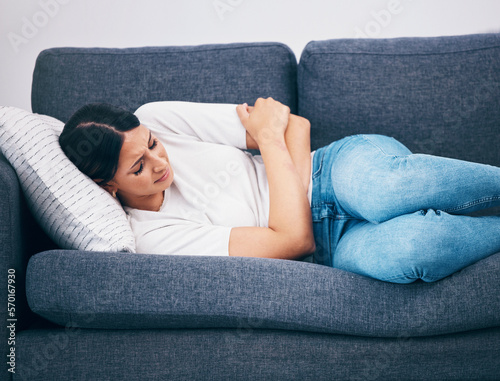 Sick, menstruation and woman with cramps on the sofa, digestion problem and pain after eating. Healthcare, hungry and girl with constipation, abdomen ulcer and stomachache from a diet on the couch © Rene La/peopleimages.com