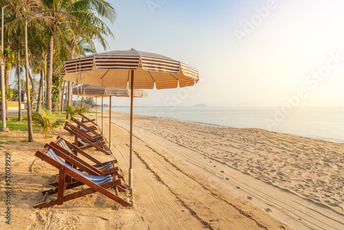 Row of empty wooden beach deck chairs with parasols on tropical sandy beach in the morning , leisure summer holidays concept 