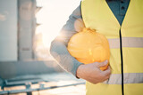 Engineering, helmet and hands of construction worker in lens flare for urban development and architecture mission. Building contractor, builder person or technician with safety gear on city rooftop
