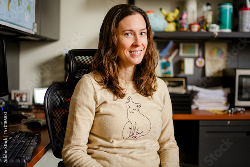 A woman professor sits at her office desk smiling with direct gaze photo