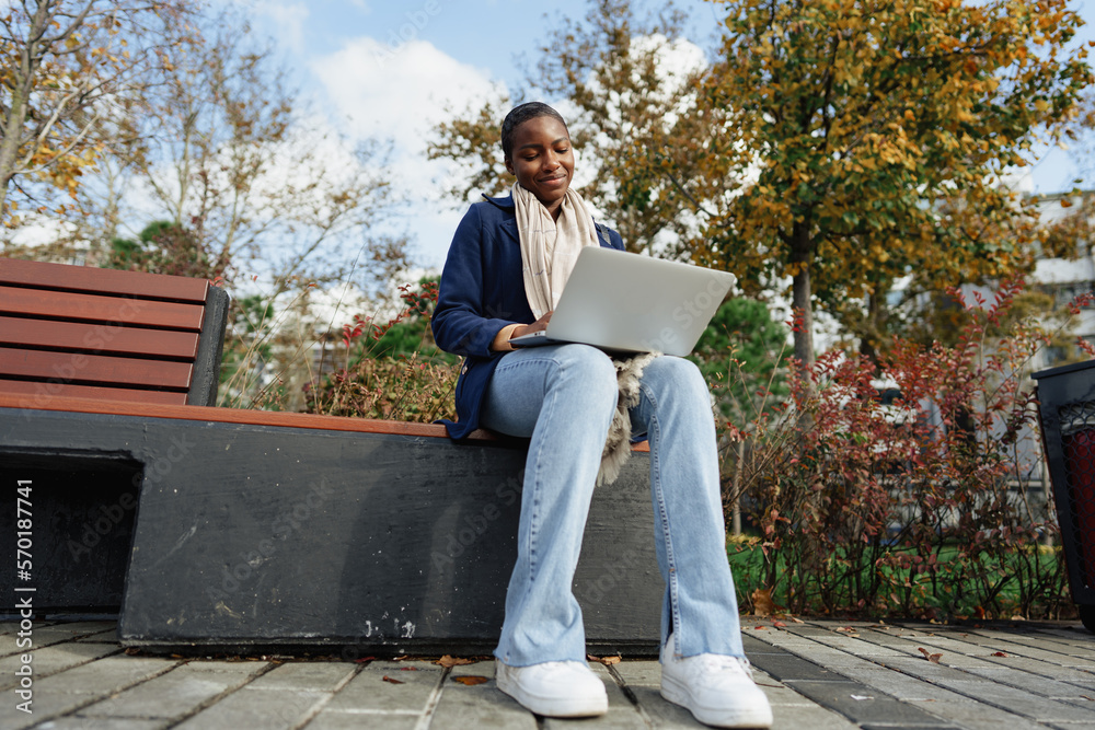 Obraz premium Young african businesswoman using laptop while sitting on the bench in the city