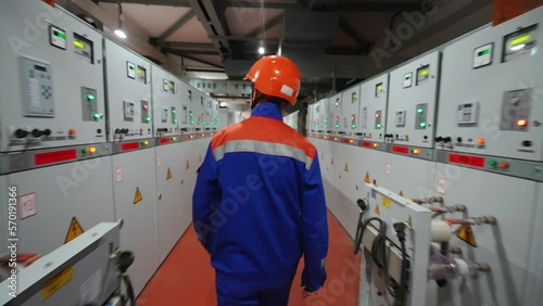 Back view, an anonymous electrician specialist walking inside the power station, an electrical engineer checking the equipment.