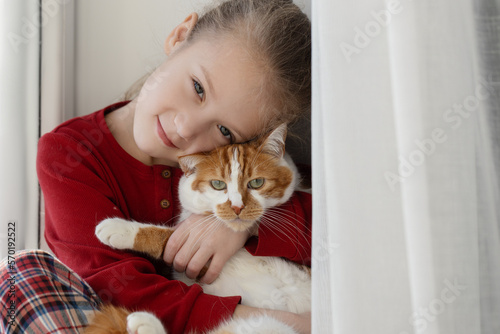 A small cute child gently embraces a red fluffy cat