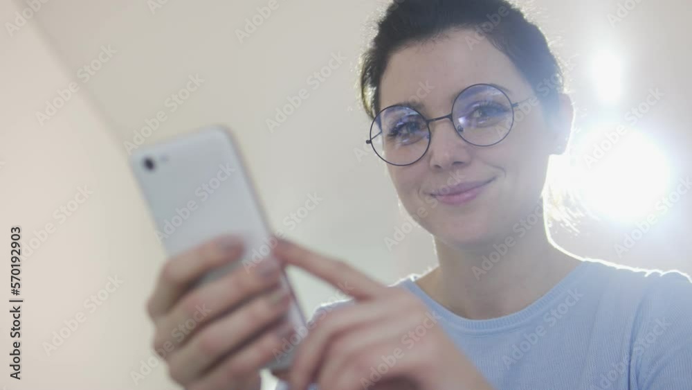 Young satisfied woman holding smartphone in hands and smiling looking at camera, using banking application, easy access to cards, payments and private documents, digitalization Young satisfied woman holding smartphone in hands and smiling looking at camera, using banking application, easy access to cards, payments and private documents, digitalization
