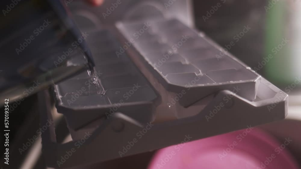 close up view of clean clear water being poured from filter into ice container. Filling ice cubes in kitchen, concept for making homemade cocktails or cooling soda drinks.