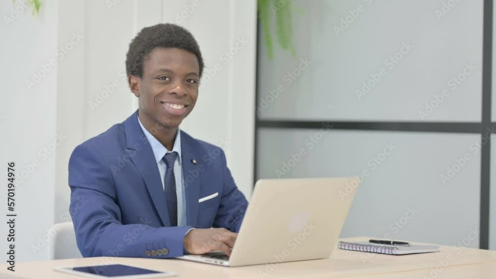 African Businessman Smiling at Camera while using Laptop African Businessman Smiling at Camera while using Laptop