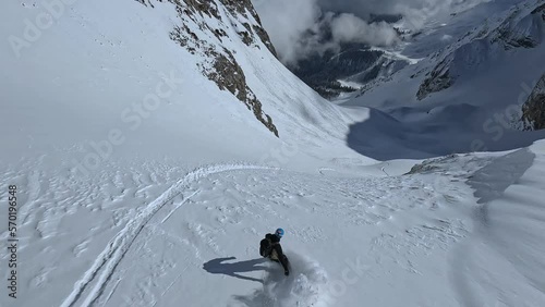 Group extreme rider flying helicopter on wild mountain snow summit ski tour north valley aerial FPV follow view. Male snowboarding riding freeride on fresh slope downhill fast dangerous heliski sport photo