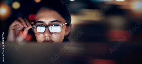 Woman, glasses reflection and computer at night for planning, website search and technology. Face of female working late on desktop, dark office and reading online network, focus vision and internet photo