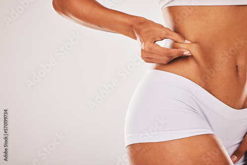 Fat, weight and woman touching her stomach isolated on a grey studio background with mockup space. Skin, cellulite and hands of a model feeling her body for insecurity, health and tummy tuck photo