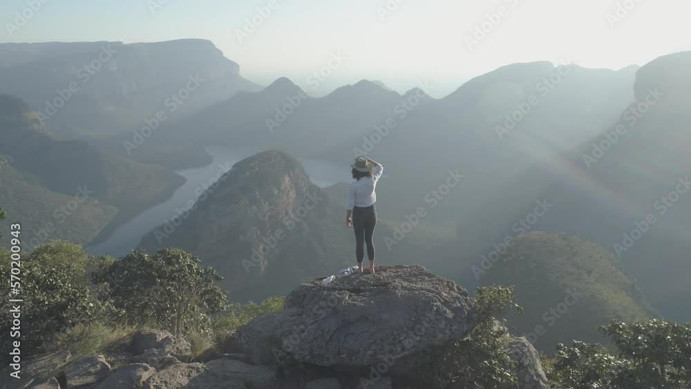 Panning shot of woman photographing while sitting on cliff at Blyde River Canyon during sunny day