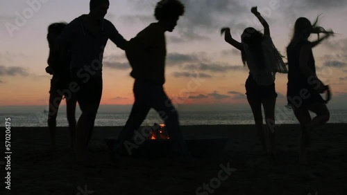 Silhouetted friends dancing around campfire at the beach photo
