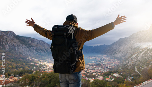 A traveler with a backpack stands on the top of the mountain and holds his hands to the sides 