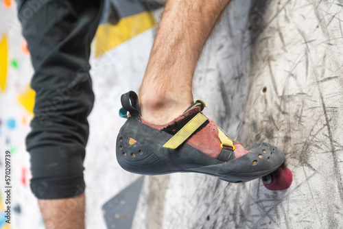 Close up view of young man or climber feet in climbing shoes on artificial indoor wall at climbing center, sport activity concept