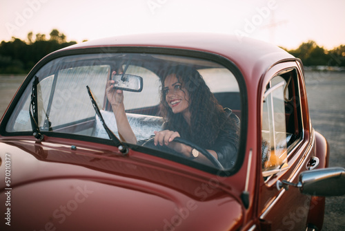 Woman sitting in her vintage car and smiling while adjusting