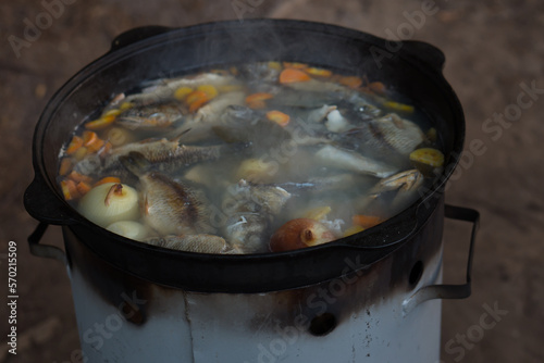 Cooking fish soup in cauldron on campfire outdoors - camp food