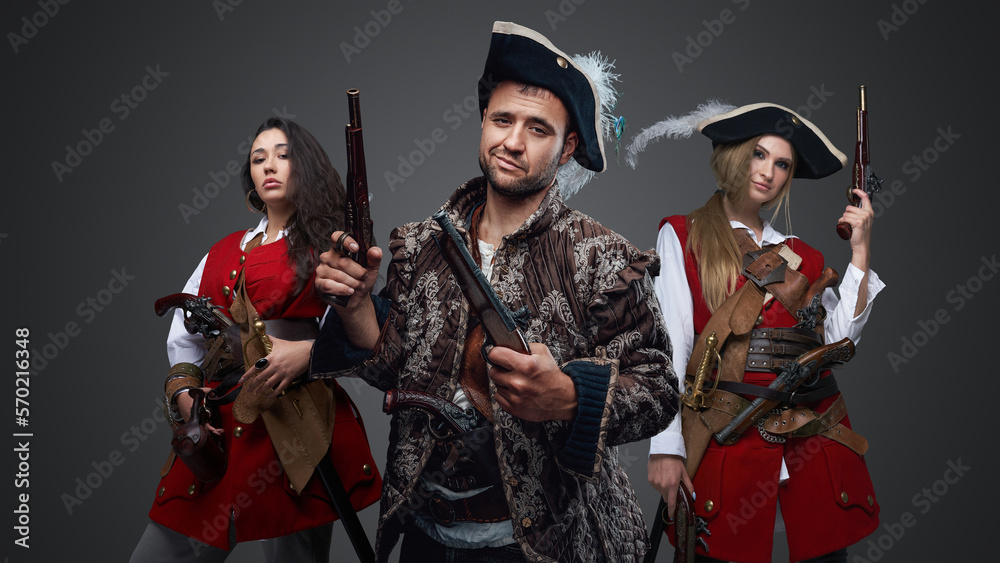 Naklejka premium Shot of pirate man and two women with flintlock guns against grey background.
