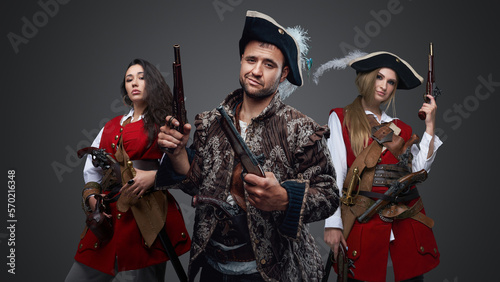 Shot of pirate man and two women with flintlock guns against grey background. © Fxquadro
