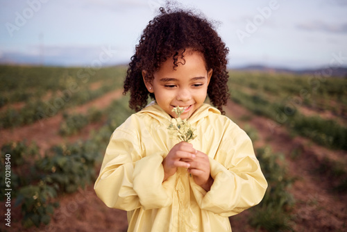 Children, farm and a girl smelling flowers outdoor in a field for agriculture or sustainability. Kids, nature and spring with a female child holding a flower to smell their aroma in the countryside photo