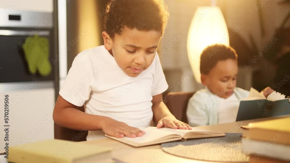 Portrait of cute little african american boy hold book and try to make homework with his younger brother at home Adorable children with developmental textbooks indoors Portrait of cute little african american boy hold book and try to make homework with his younger brother at home Adorable children with developmental textbooks indoors