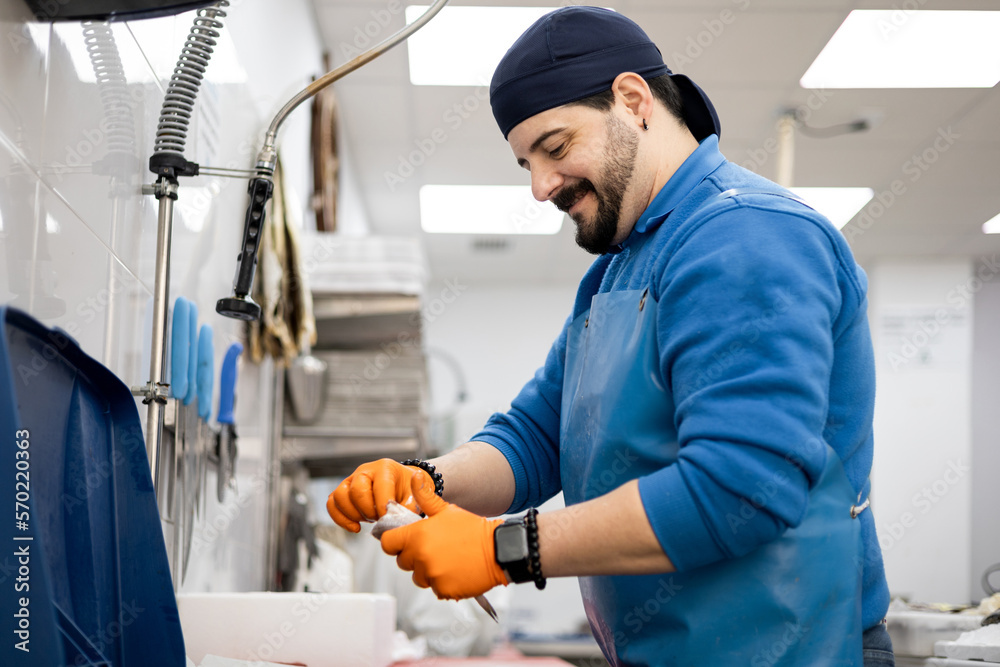 A middle-aged fishmonger cleans a fish with his back to the sales counter, selling food, a small and medium-sized business concept. A middle-aged fishmonger cleans a fish with his back to the sales counter, selling food, a small and medium-sized business concept.