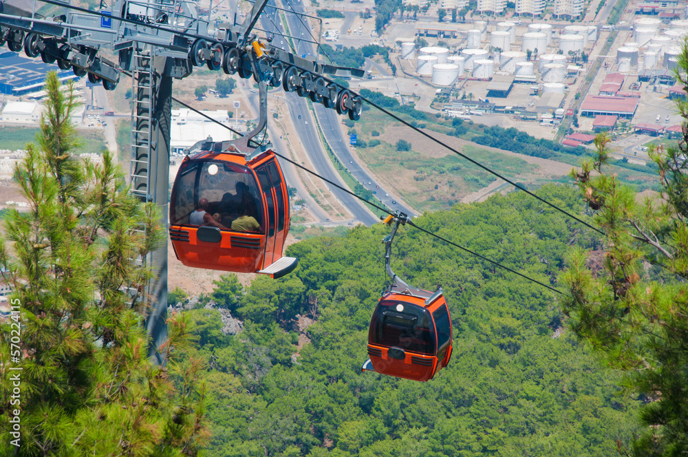 Red funicular railway cabins climbing to mountains under big city. Green trees around