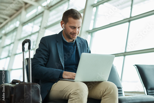 Airport, business man and laptop for music during travel or working in lobby streaming internet. Entrepreneur person with luggage in building for video call while typing email, search or news