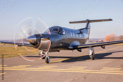 The plane is traveling on the taxiway, its propeller is spinning. Single turboprop aircraft on runway in sunny day.