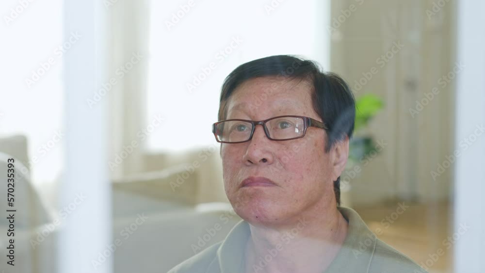 Lonely senior asian man, siting alone in the room, looking through the window Lonely senior asian man, siting alone in the room, looking through the window